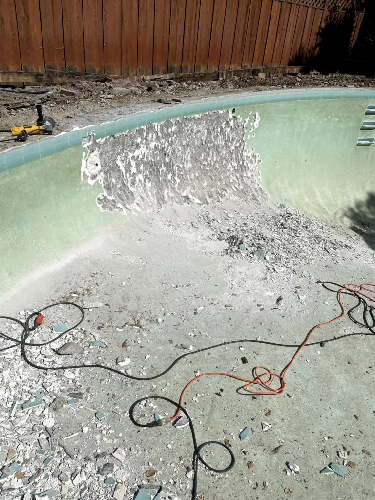 A swimming pool is being repaired by a man with a shovel.