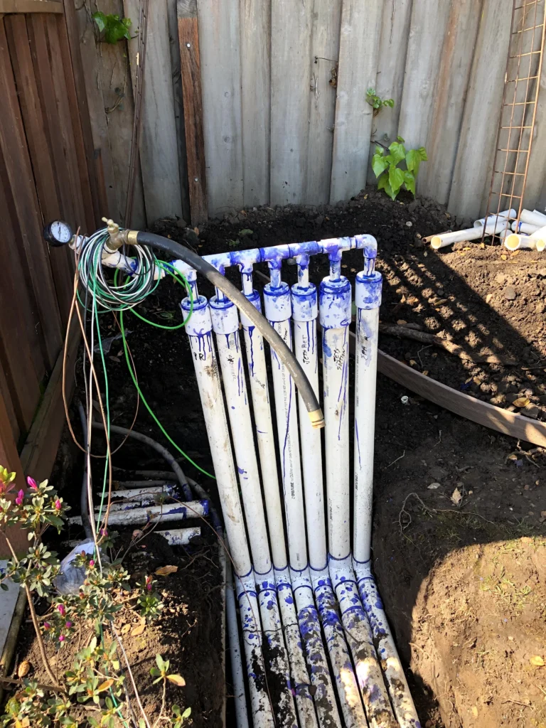 A radiator in a garden with hoses attached to it.